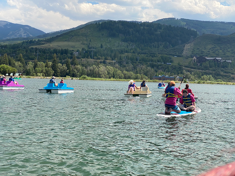 More Paddleboarders and Pedal boaters on lake with view of mountains in distance