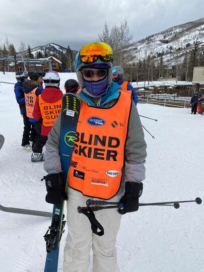 Blind skier wearing ski gear holding skis and poles