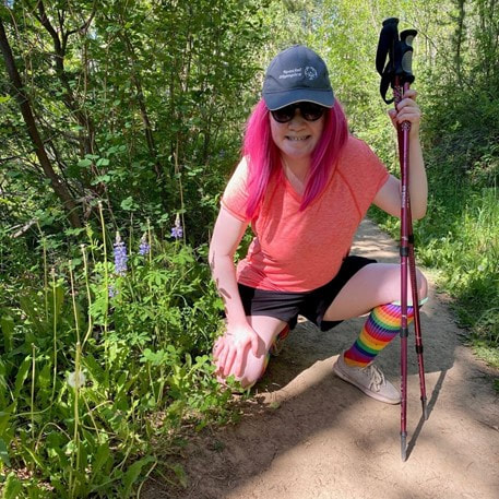 Jazmine in baseball cap, crouched and holding walking sticks