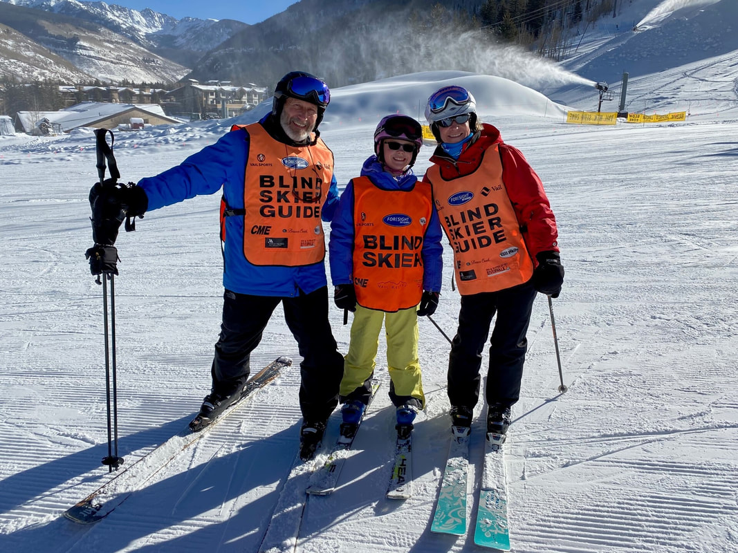 Blind skier posing with 2 guides in ski gear