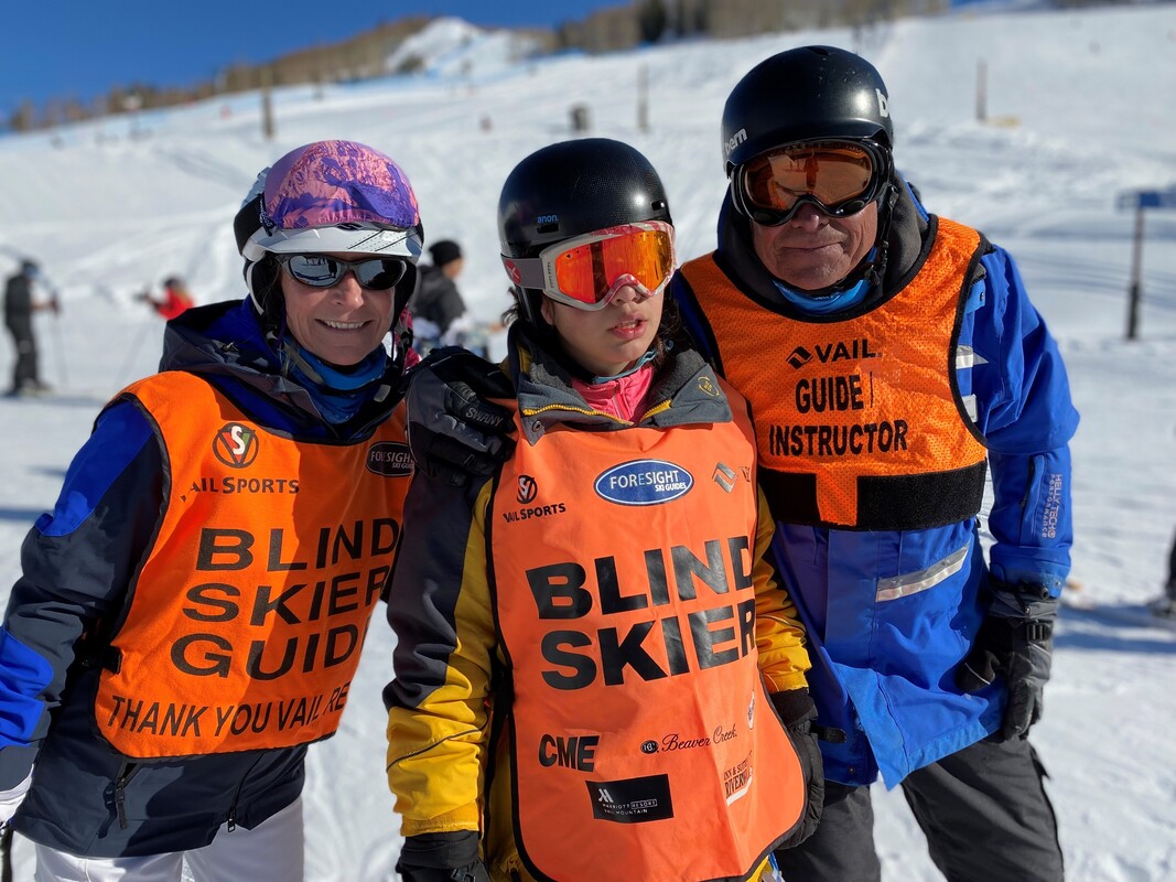Blind skier posing with guide and guide instructor in ski gear