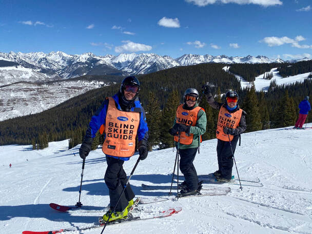 Blind skier and two guides in ski gear on mountain
