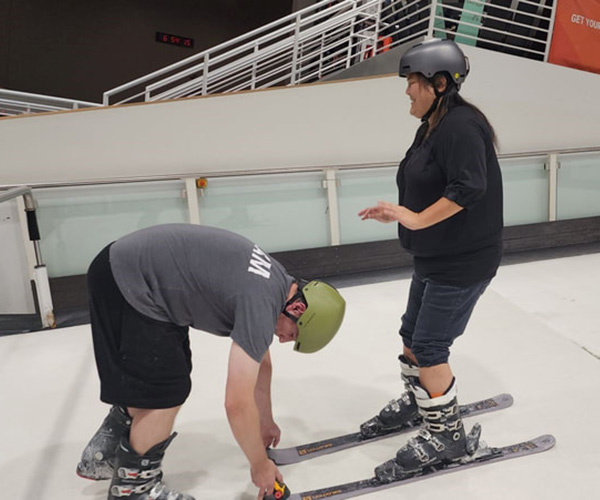 Woman standing in skis on indoor ski slope being assisted by guide