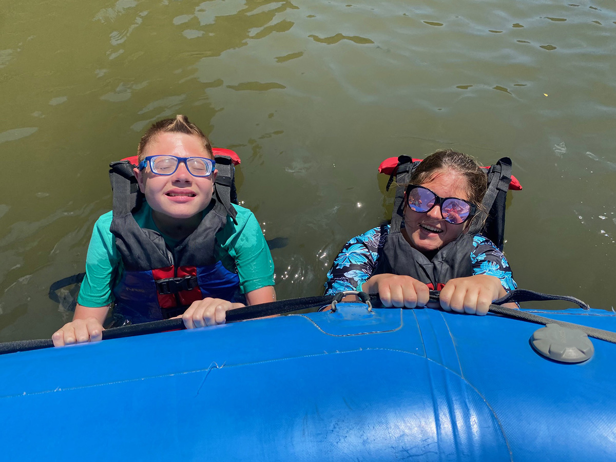 Two campers in the river holding on to side of boat